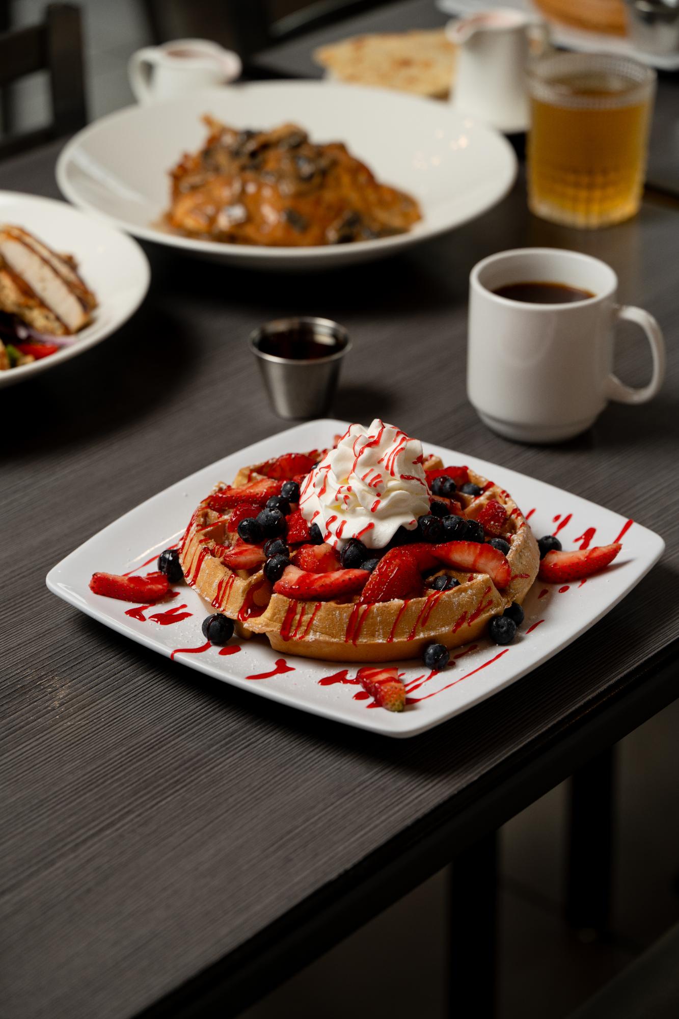 Very Berry Waffle piled with strawberries, blueberries and whipped cream, with coffee on the table
